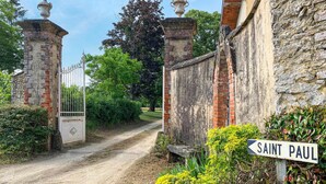 Une route de campagne menant à une entrée fermée par un portail, sur laquelle on peut lire l’inscription « SAINT PAUL ».