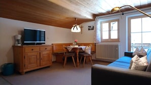 A cozy room with a wooden ceiling, a television on a cabinet, a dining table with chairs, and a sofa. - Apartment Wallberg - Böcklhof, Kreuth-Brunnbichl (Kreuth)