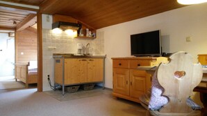 A kitchen with wooden cabinets, a sink, a coffee maker, a television, and a chair with a heart-shaped cutout. - Apartment Wallberg - Böcklhof, Kreuth-Brunnbichl (Kreuth)