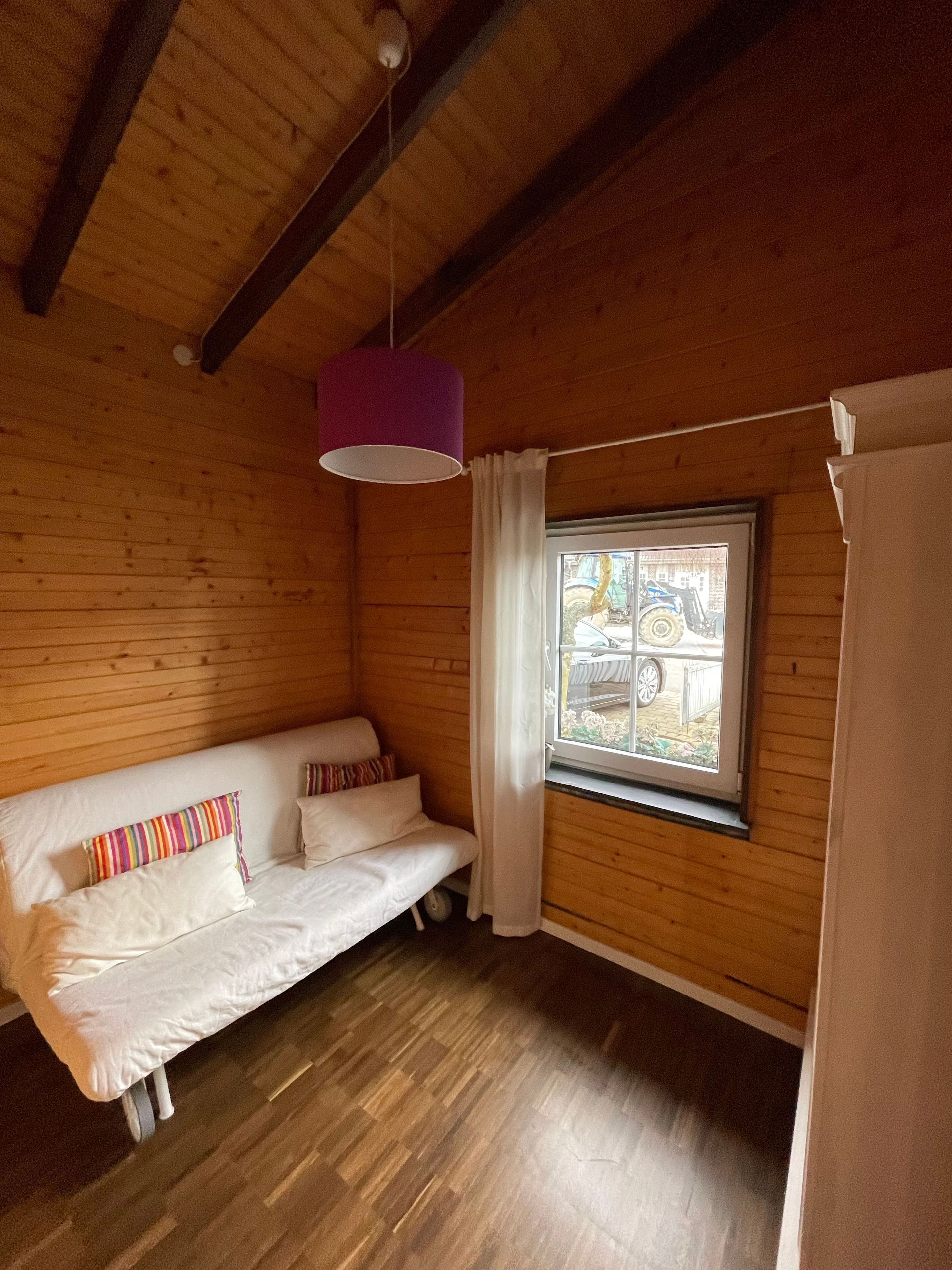 Une pièce en bois avec un lit, une fenêtre avec des rideaux et un luminaire suspendu.