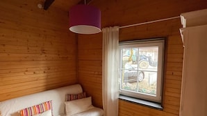 Quarto de madeira com uma cama, janela com cortinas e luminária pendente.