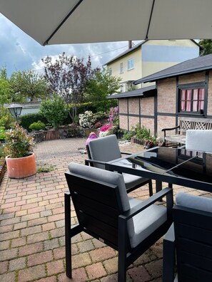 Un espace extérieur aménagé en terrasse, avec une table et des chaises, entouré d’un mur en briques et de plantes en pot.