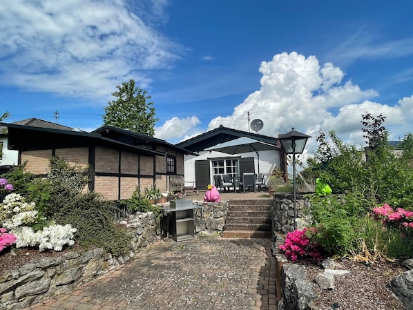 A traditional Japanese-style house with a stone pathway leading to a covered patio area. - Cozy Eifelhäuschen in the green near Nürburgring - (Hoffeld)