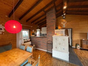 Un intérieur en bois avec une cheminée en briques, un coin repas avec une table et des chaises en bois, et un luminaire rouge suspendu.