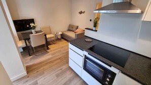 Una cocina moderna con horno empotrado, comedor con mesa y sillas, y un pequeño rincón de descanso con sofá.