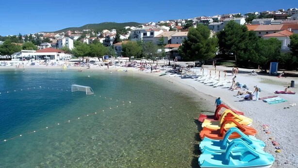 Una playa con aguas cristalinas, una hilera de toboganes acuáticos coloridos y un pueblo al fondo.
