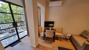 Una sala de estar moderna con un ventanal grande, un televisor de pantalla plana, un sofá y una zona de comedor con sillas.