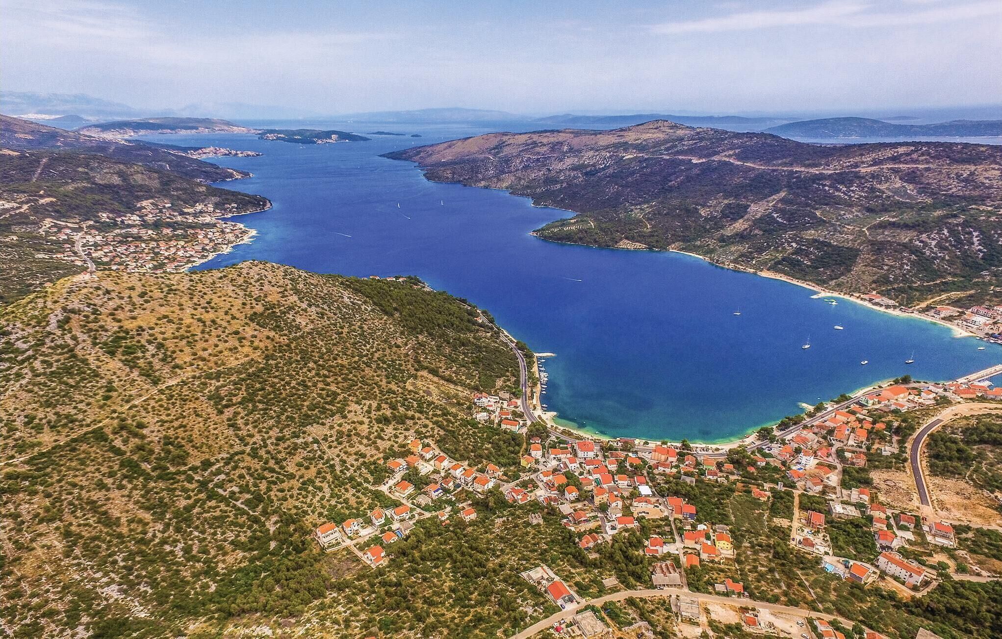 Vista aérea de un pueblo costero con un puerto deportivo, rodeado de colinas y una extensa masa de agua.
