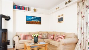 A cozy living room with a beige sofa, striped pillows, a glass coffee table, a fireplace, a bookshelf, and a painting on the wall. - Rasmus 1 from A&M - Rasmus 1 (Kampen (Sylt))