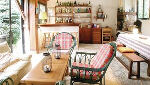 A cozy interior with wicker chairs, a wooden table, and a bar area with shelves of bottles and glasses. - Awesome home in Ustaritz (Ustaritz)