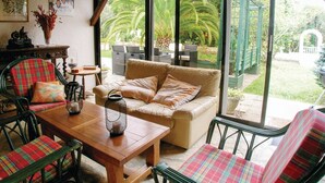 A cozy patio area with a wooden table, plaid chairs, a beige sofa, and a view of a garden with palm trees. - Awesome home in Ustaritz (Ustaritz)
