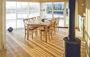Un comedor con mesa y sillas de madera, ventanas amplias con vistas a un paisaje nevado y un estufa de leña.