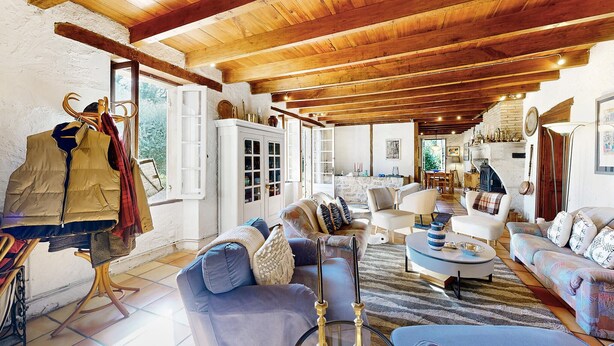 Ein geräumiges Wohnzimmer mit Holzbalken, einem Kamin und unterschiedlichen Sitzmöglichkeiten, darunter Sofas und Sessel.