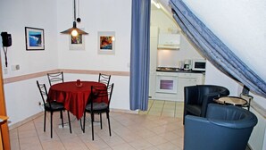 A dining area with a red table and four chairs, a kitchen in the background, and a blue curtain. - Apartment 02 - Guesthouse Captain Winston (Putbus)