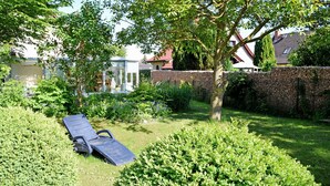 A garden with a sun lounger, a stone wall, and a tree. - Apartment 02 - Guesthouse Captain Winston (Putbus)