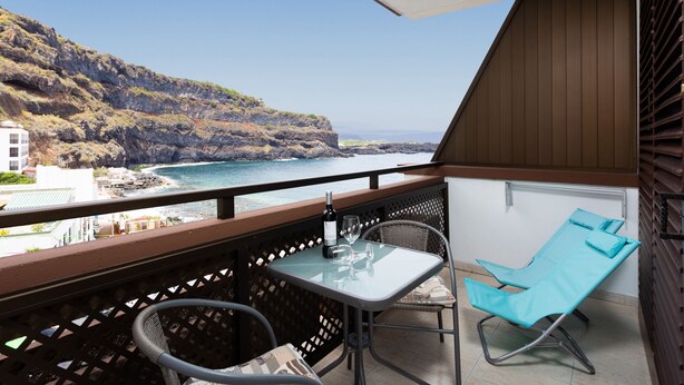 A balcony with a table and chairs overlooking a coastal view.