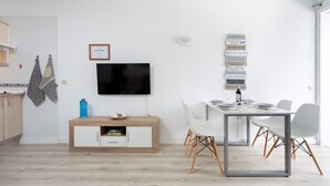 A modern kitchen with a flat-screen TV, a dining table with chairs, and a cabinet with a blue water bottle on it.