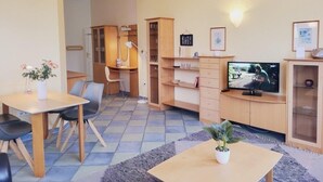 Un espace de vie compact comprenant un coin repas, un téléviseur et une petite bibliothèque.