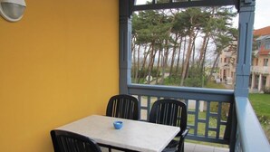 Un balcon avec une table et des chaises, une vue sur les arbres et les bâtiments, et un mur jaune.