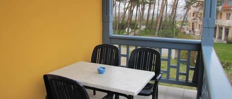 A balcony with a table and chairs, a view of trees and buildings, and a yellow wall.