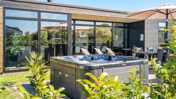 En moderne udendørs terrasse med jacuzzi, glasvægge og udendørs møbler.