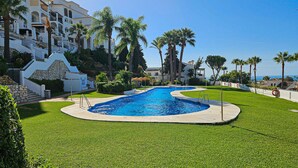 A swimming pool surrounded by well-maintained grass, palm trees, and a white building with multiple balconies. - El mirador de Calahonda (Calahonda)