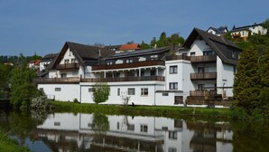Un immeuble à plusieurs étages doté de balcons, qui se reflète dans l’eau, sous un ciel dégagé.
