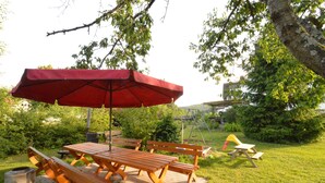 Une terrasse extérieure avec des tables et des bancs en bois, un parasol rouge et une balançoire.
