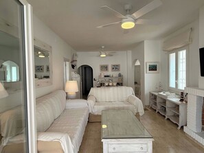 A room with a white sofa, a glass-top coffee table, a white cabinet, and a ceiling fan.