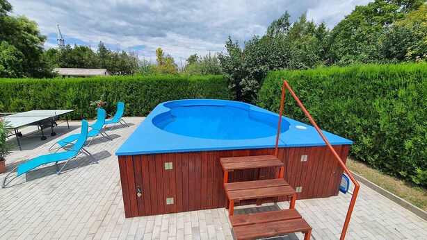 A swimming pool with a wooden deck, a slide, and a table tennis table.