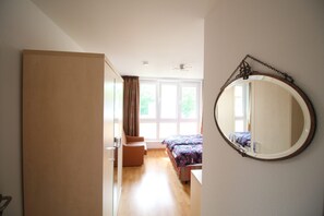 A bedroom with a bed, a chair, a wardrobe, a large window, and a mirror on the wall.