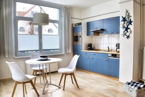 Eine kleine Küche mit blauen Schränken, einem runden Esstisch, weißen Stühlen und einer Pendelleuchte.