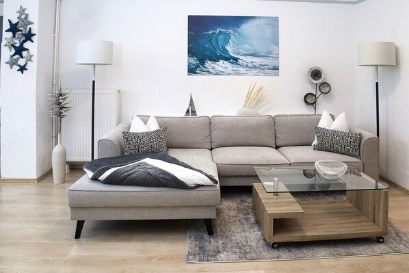 Ein modernes Wohnzimmer mit einer Eckcouch, einem Glastisch und Dekorationselementen.