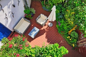 Eine Terrasse mit Sitzgelegenheit, eine blaue Tür und ein Garten mit verschiedenen Pflanzen und Blumen.