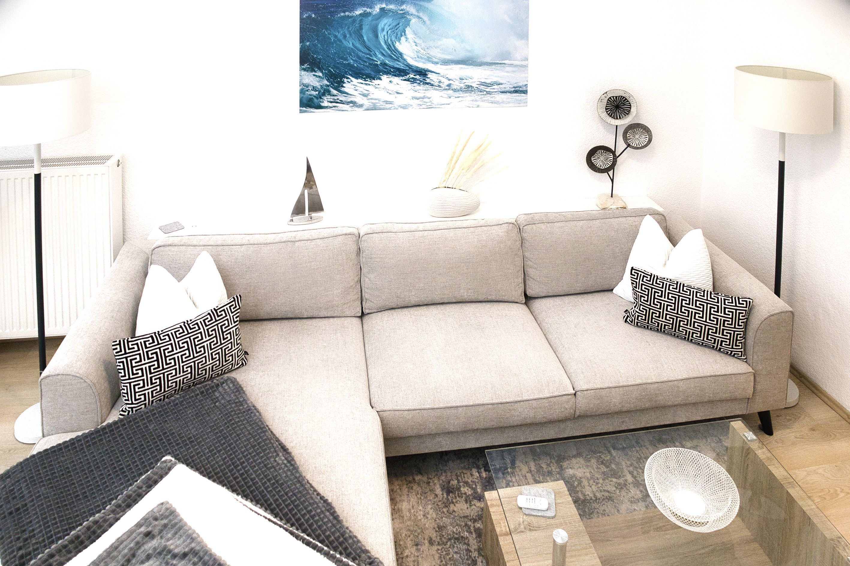 A living room with a sofa, two patterned pillows, a small decorative sailboat, a vase with reeds, a wall-mounted picture, and a floor lamp.