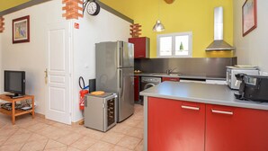 Cocina compacta con refrigerador, estufa y lavaplatos. Se observa una lavadora pequeña y un televisor sobre una mesa de madera.