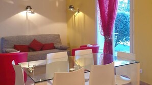 Una sala de estar con un sofá, cojines rojos, una mesa de centro de vidrio y dos lámparas fijadas a la pared.