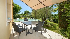 Un patio al aire libre con mesa y sillas, una piscina y un jardín.