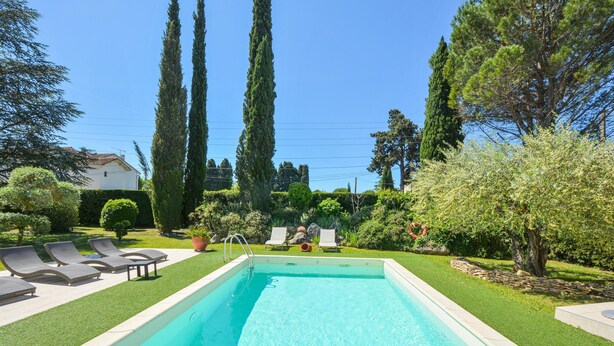 Una piscina con sillas de descanso, rodeada de follaje cuidado y árboles altos.