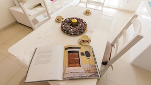 Un coin repas avec une table blanche, un livre ouvert posé dessus et une couronne décorative sur la table.