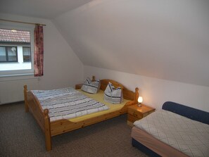 Ein Schlafzimmer mit einem hölzernen Bett, einem Nachttisch mit Lampe, einem Fenster mit Vorhängen und einer Heizung.