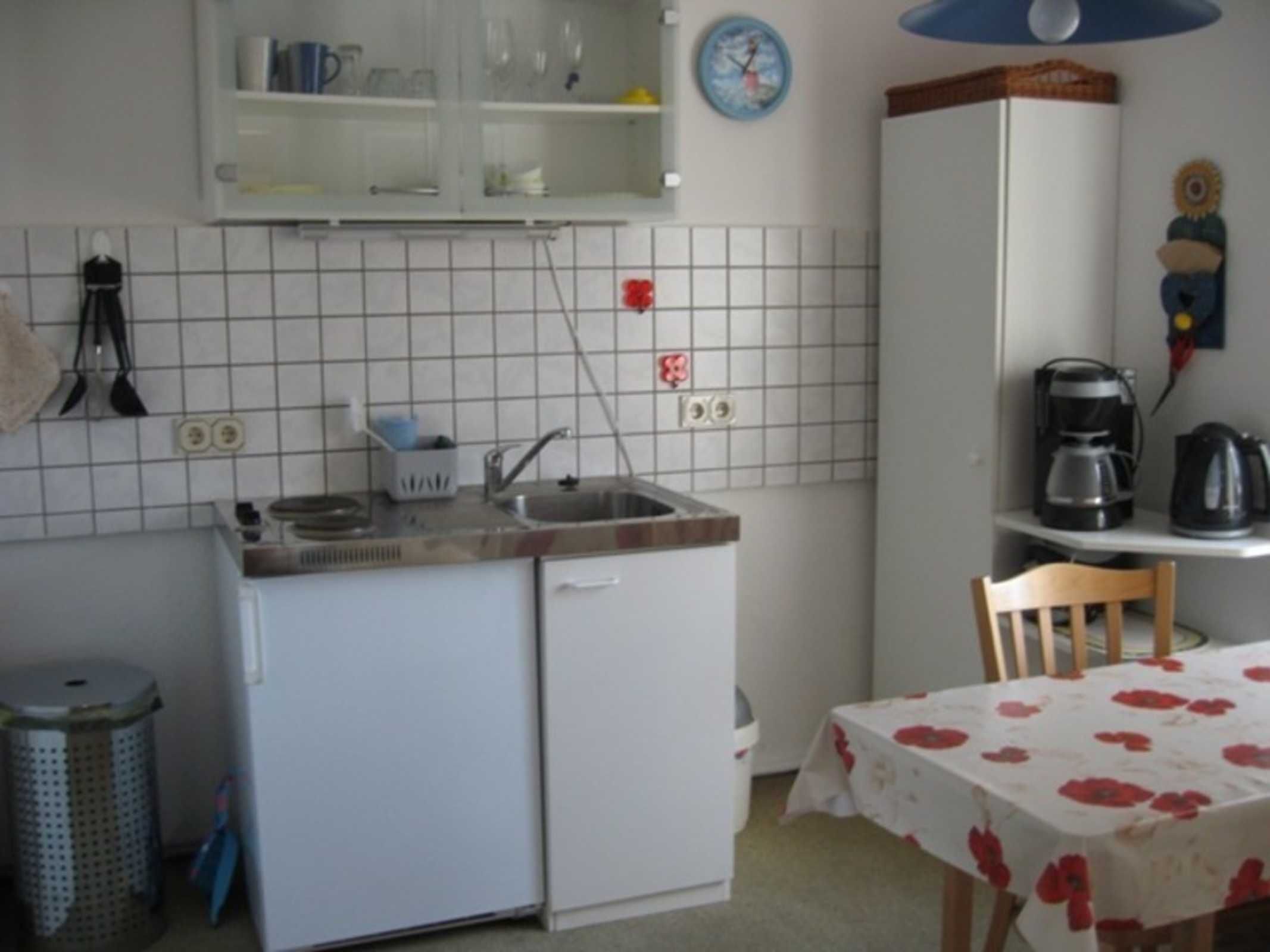 A compact kitchen with a sink, a small refrigerator, a coffee maker, and a dining table with a floral tablecloth.