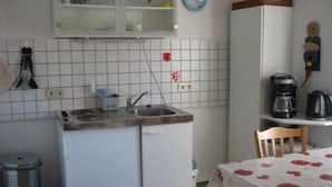 Una cocina compacta con un lavamanos, un refrigerador pequeño, una cafetera y una mesa de comedor con mantel floreado.