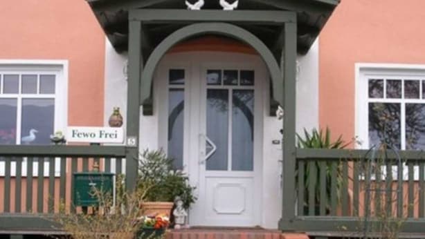 Un edificio con puerta blanca, un pequeño porche con barandal verde y un letrero que dice