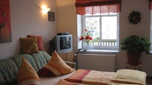 Una sala de estar acogedora con un sofá, dos camas con ropa de cama a juego, un televisor, una ventana con vistas y una planta en maceta.