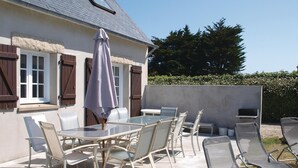 Une terrasse extérieure avec une table et des chaises en verre, un parasol et un barbecue.