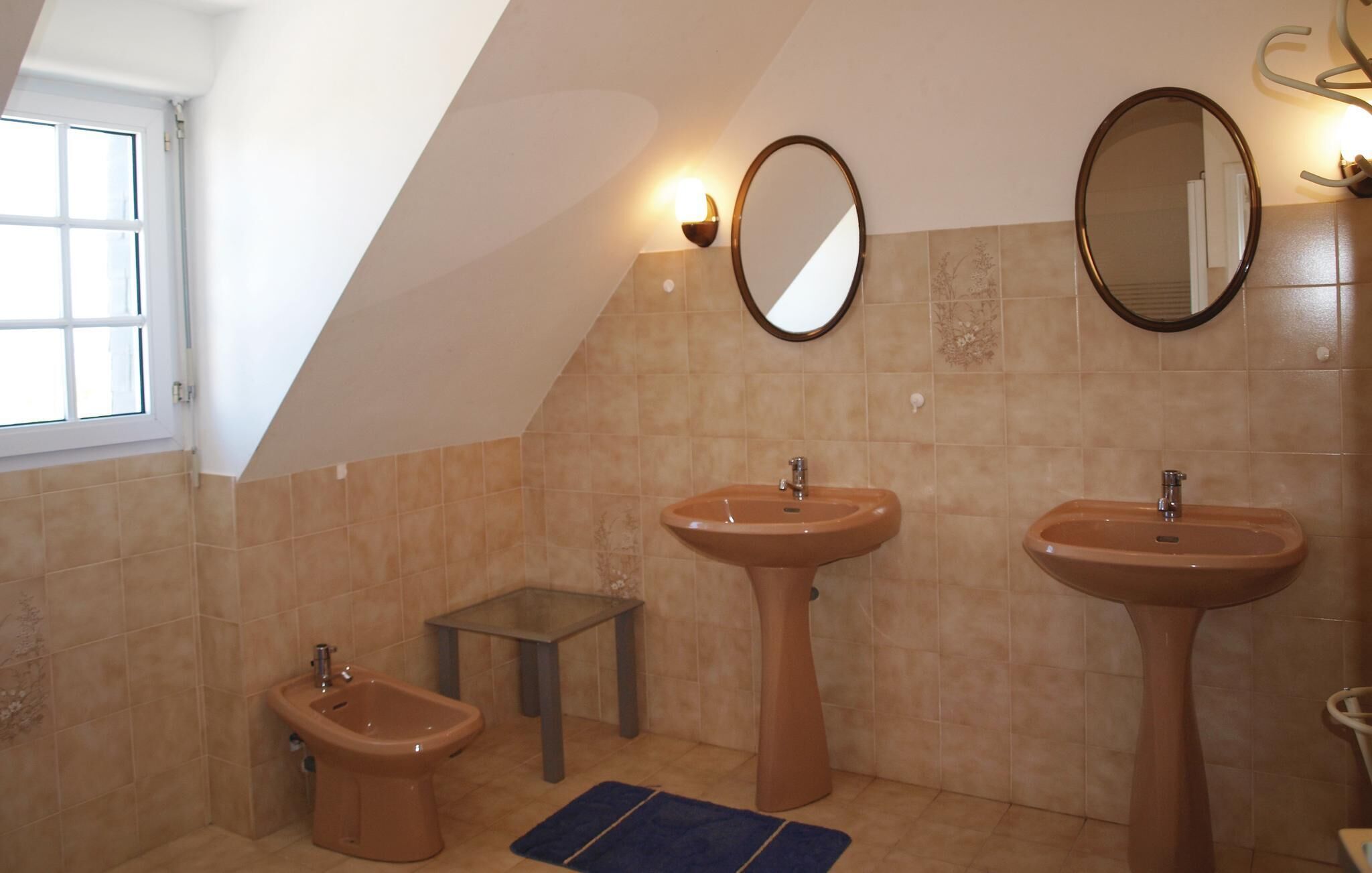 A bathroom with two sinks, a bidet, and a small table.