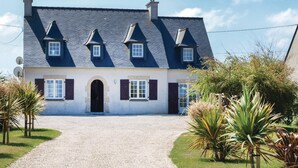 Une maison à deux étages avec une allée gravillonnée, une entrée centrale et un jardin agrémenté de palmiers.