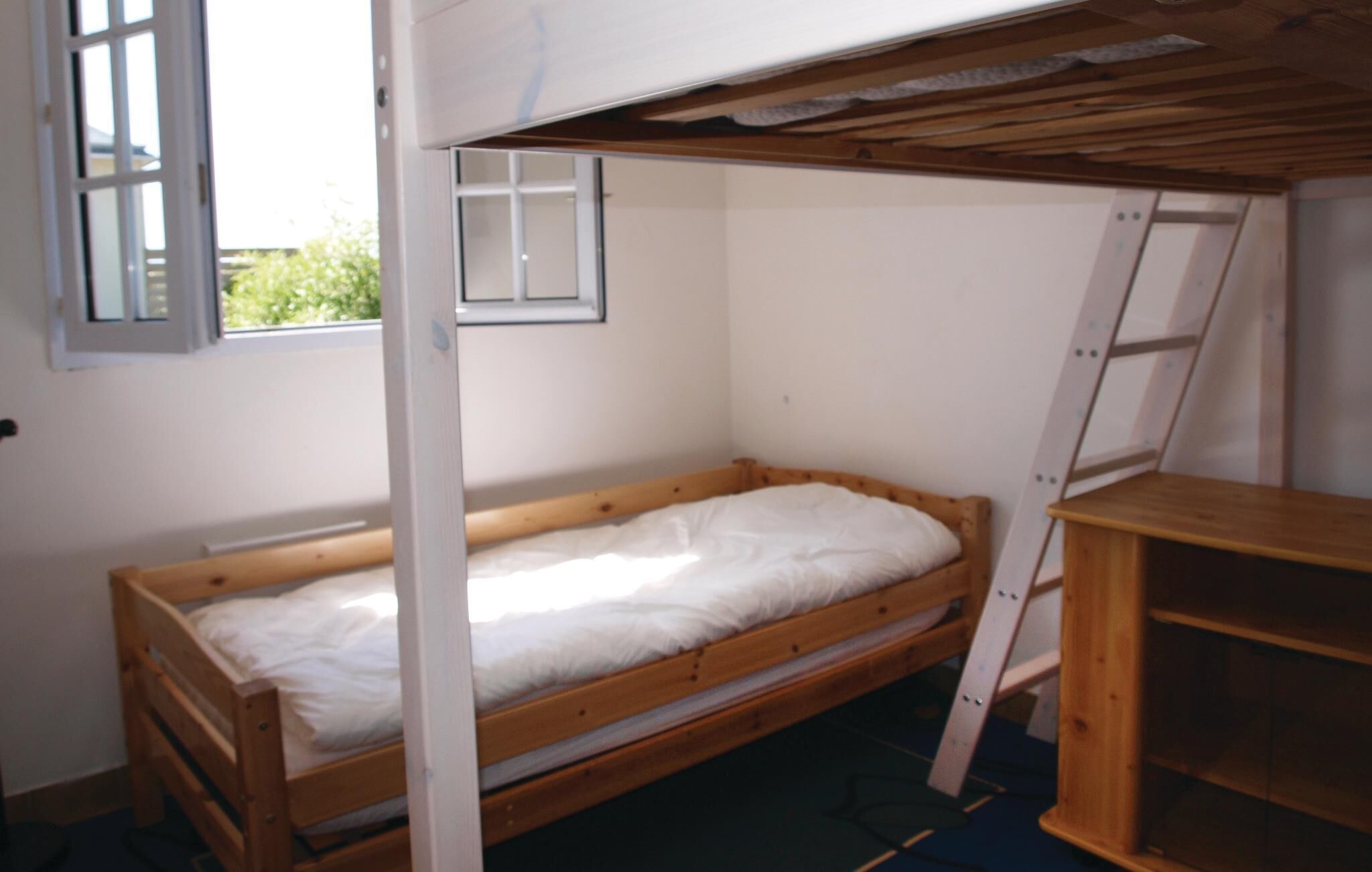 Een kleine kamer met een enkel bed en een houten stapelbed, een raam en een ladder.