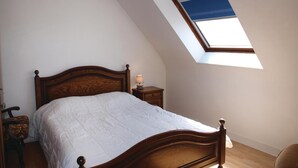 Une chambre à coucher avec un lit en bois, une table de chevet, une lampe et une lucarne.